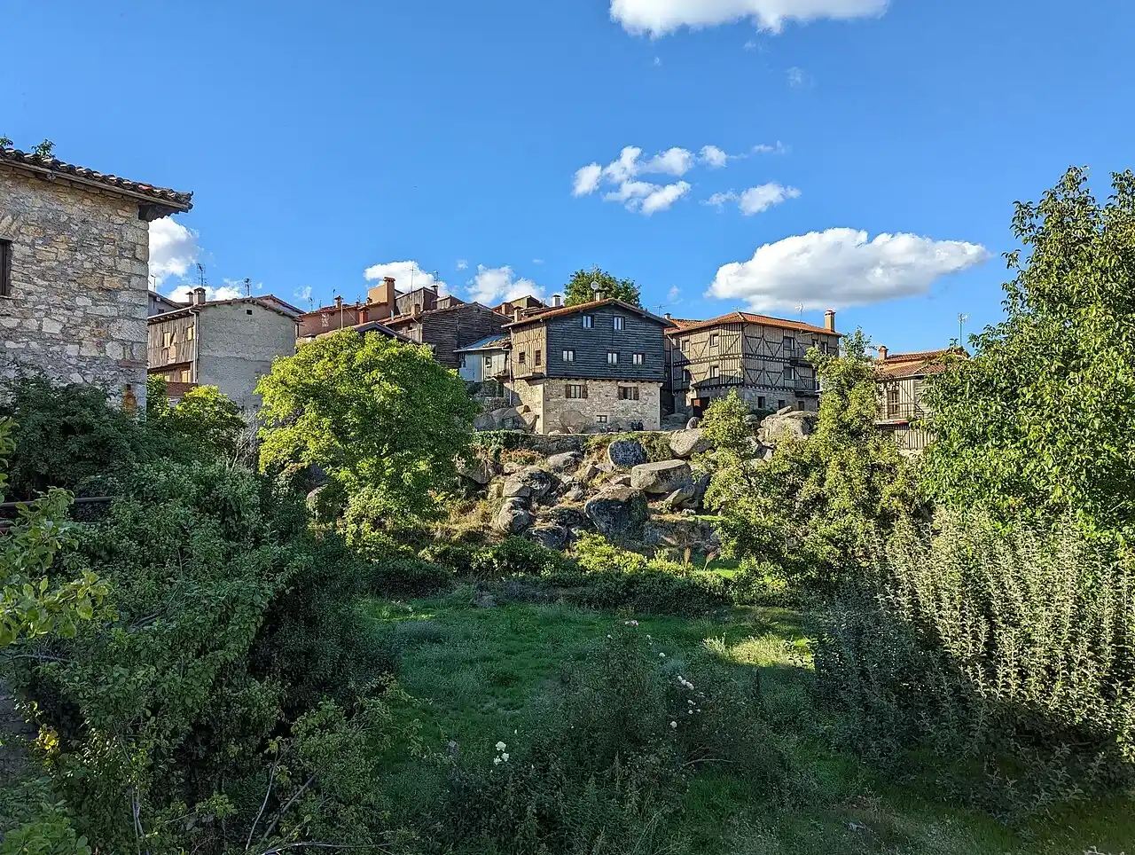 Mudanzas en La Alberca 8 Casas de piedra y entramado de madera sobre un cerro de rocas, rodeadas de árboles, con el cielo azul al fondo